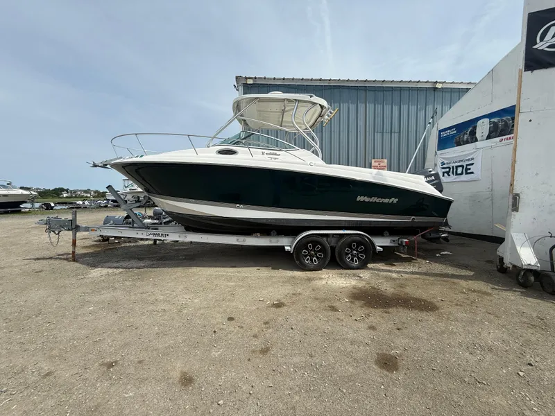 Slide: The Image of 2005 Wellcraft 252 Coastal boat on trailer, parked outdoors near a metal building. - 2