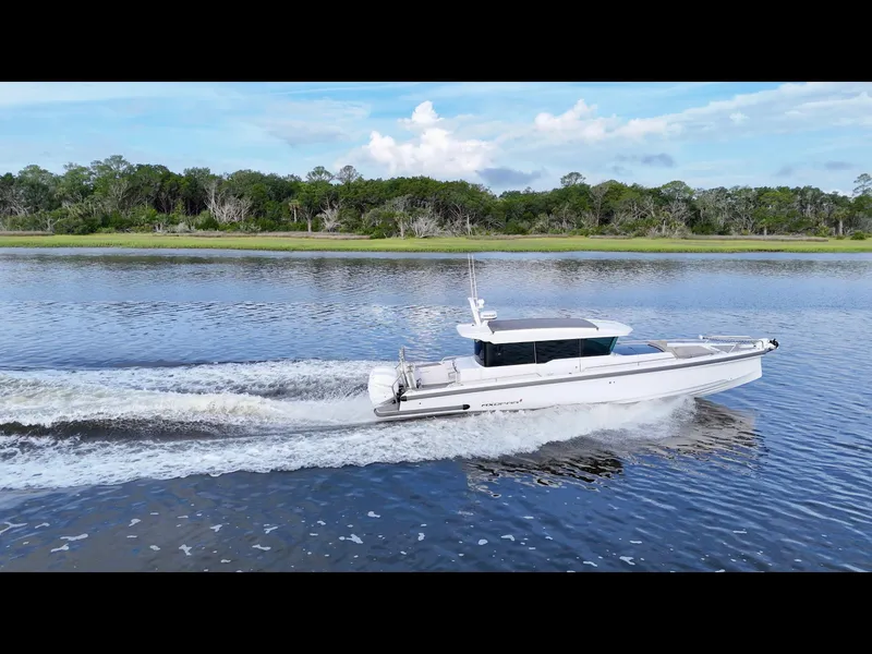 Slide: The Image of 2023 Axopar 37 Cross Cabin cruising on a serene lake with lush green shoreline. - 3