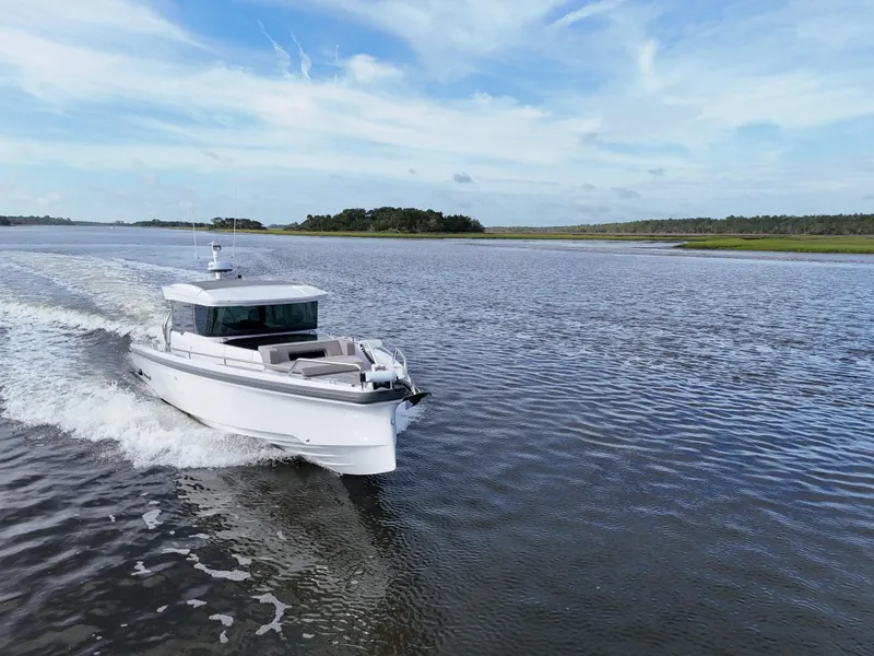 Slide: The Image of 2023 Axopar 37 Cross Cabin cruising on a serene waterway under a clear blue sky. - 5