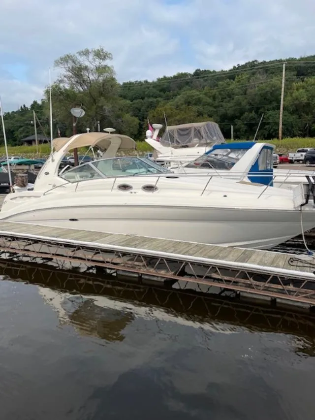 The Image of 2004 Sea Ray 320 Sundancer docked at a marina, surrounded by lush greenery. - 0