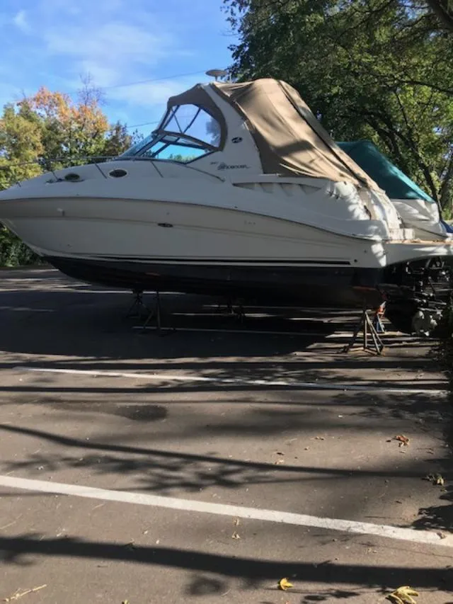 Slide: The Image of 2004 Sea Ray 320 Sundancer boat on stands in a parking lot, surrounded by trees. - 5