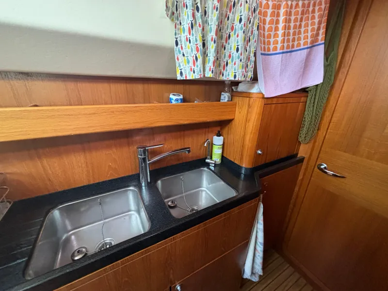 Slide: The Image of Double sink in a 2014 Southerly 535 yacht kitchen with wooden cabinetry and colorful curtains. - 31