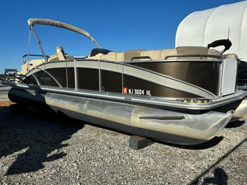 Slide: The Image of 2018 Sylvan S3 pontoon boat on gravel, featuring beige seating and canopy. - 2