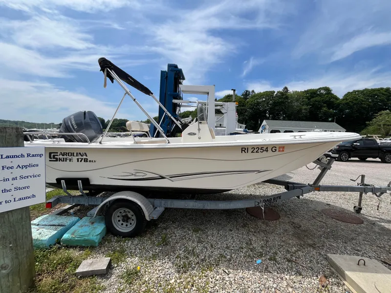 Slide: The Image of 2013 Carolina Skiff 178 DLV boat on trailer, parked outdoors under a blue sky. - 3