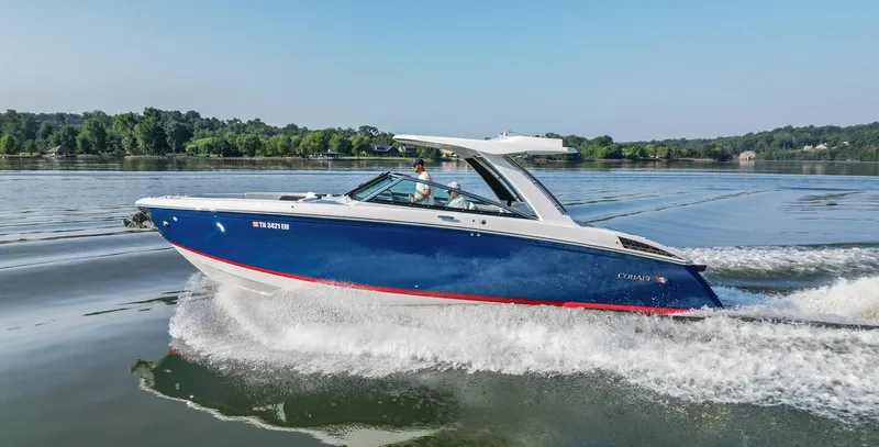 Slide: The Image of 2023 Cobalt R33 boat cruising on a serene lake with lush green shoreline. - 2
