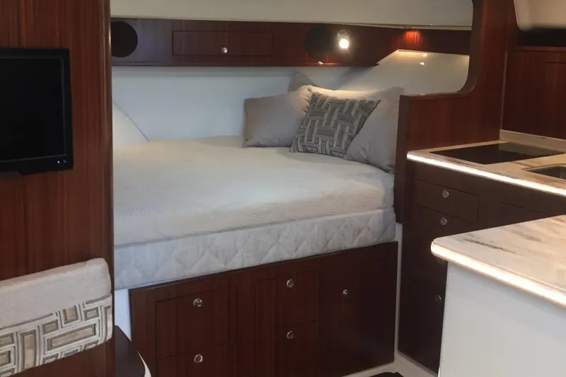 Slide: The Image of 2021 Pursuit OS 385 Offshore cabin interior with bed, wood cabinetry, and kitchenette. - 19