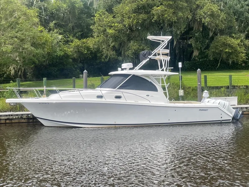 Slide: The Image of 2021 Pursuit OS 385 Offshore boat docked by lush greenery. - 2