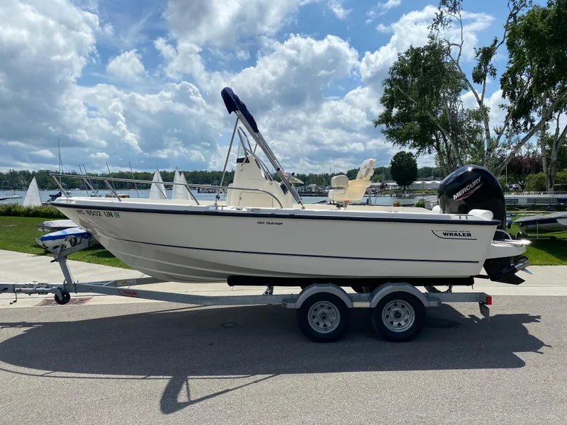 Slide: The Image of 2021 Boston Whaler 190 Outrage boat on trailer, parked near marina under cloudy sky. - 3