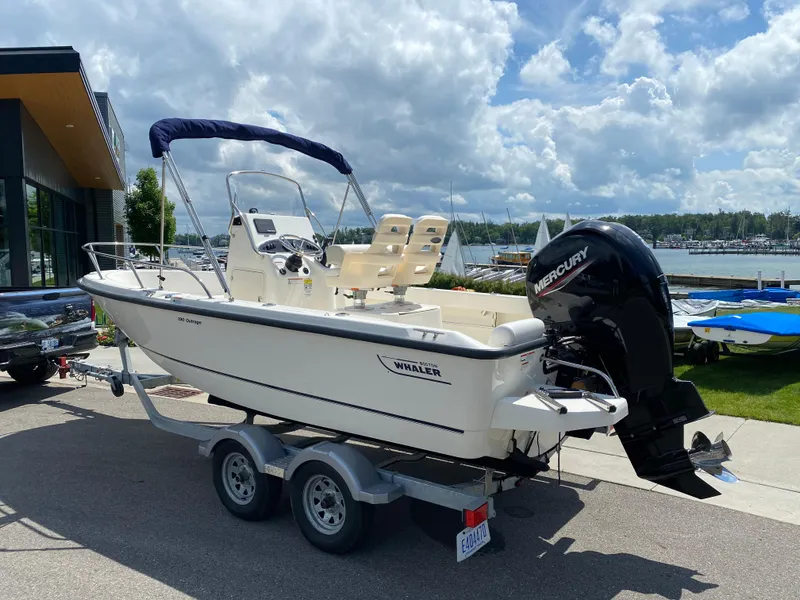 Slide: The Image of 2021 Boston Whaler 190 Outrage boat on trailer, parked near marina under cloudy sky. - 4