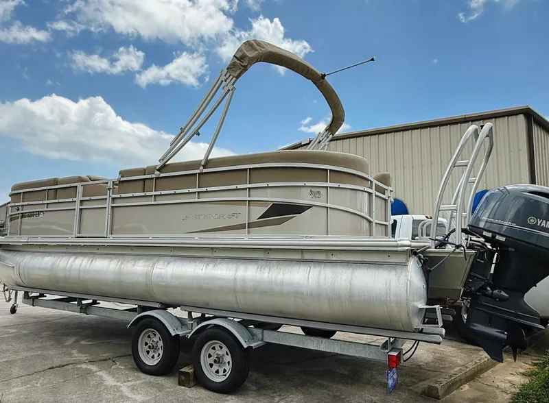 Slide: The Image of 2022 Starcraft LX22 pontoon boat on trailer, parked outdoors under blue sky. - 21