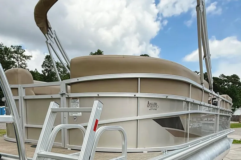 Slide: The Image of 2022 Starcraft LX22 pontoon boat with beige seating and aluminum railing under a cloudy sky. - 6