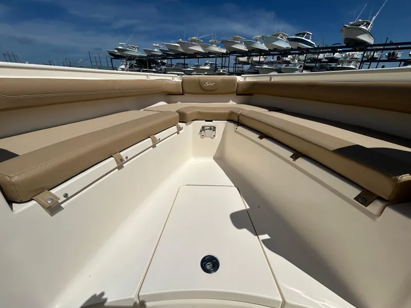 Slide: The Image of 2018 Scout 275 LXF boat interior with tan seating and storage, docked under blue sky. - 21
