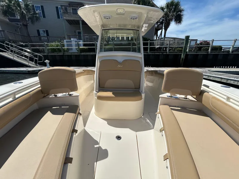 Slide: The Image of 2018 Scout 275 LXF boat interior with beige seating and console, docked near waterfront homes. - 25