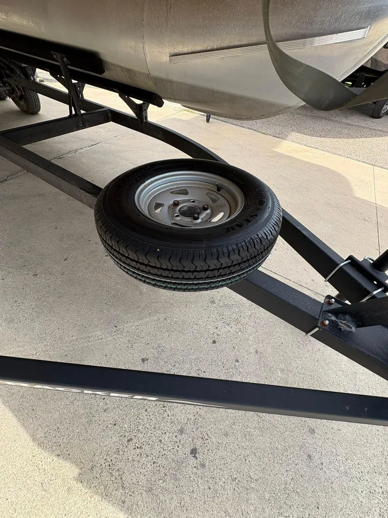 Slide: The Image of 2023 Sun Tracker Party Barge 20 DLX trailer with spare tire on concrete surface. - 4