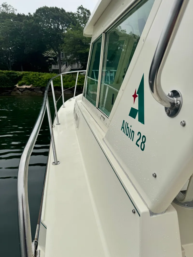 Slide: The Image of 2001 Albin 28 boat docked, featuring sleek design and railing, with lush greenery in background. - 7