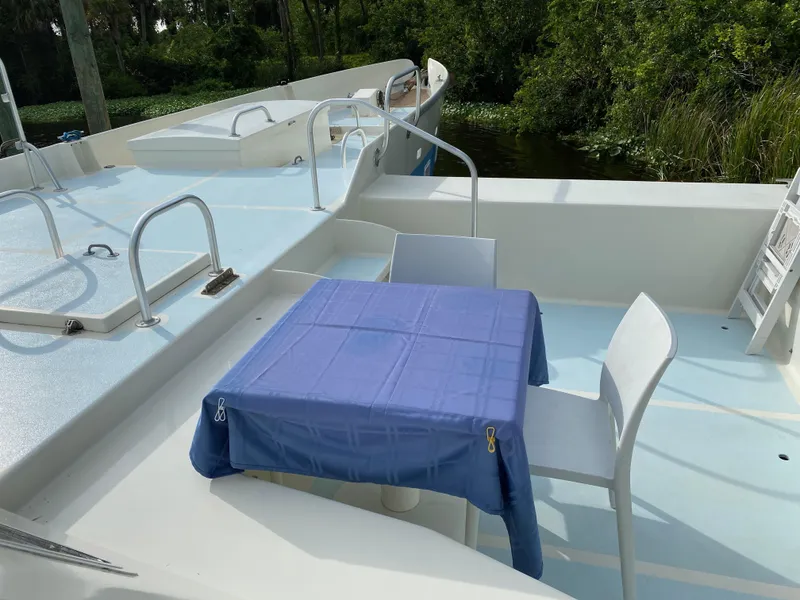 Slide: The Image of Boat deck with blue tablecloth, chairs, and lush greenery in the background. - 8
