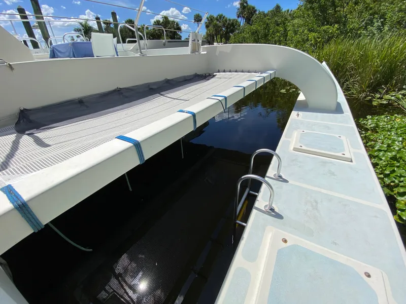 Slide: The Image of Catamaran deck with netting, Custom 62 model, 1996, docked near lush greenery. - 9