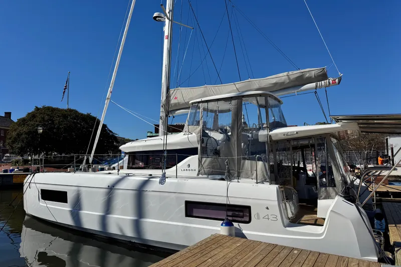 Slide: The Image of 2026 Lagoon 43 catamaran docked at a marina under clear blue skies. - 2