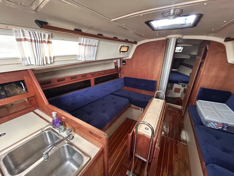 Slide: The Image of Interior of 1985 O'Day 35 sailboat with blue seating, wooden finishes, and compact kitchen area. - 17