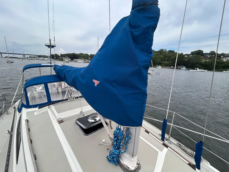 Slide: The Image of 1985 O'Day 35 sailboat deck with blue sail cover, moored in a scenic harbor. - 9