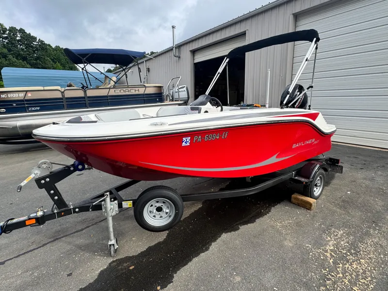 Slide: The Image of 2024 Bayliner Element M15 boat in vibrant red on a trailer, parked outdoors. - 2