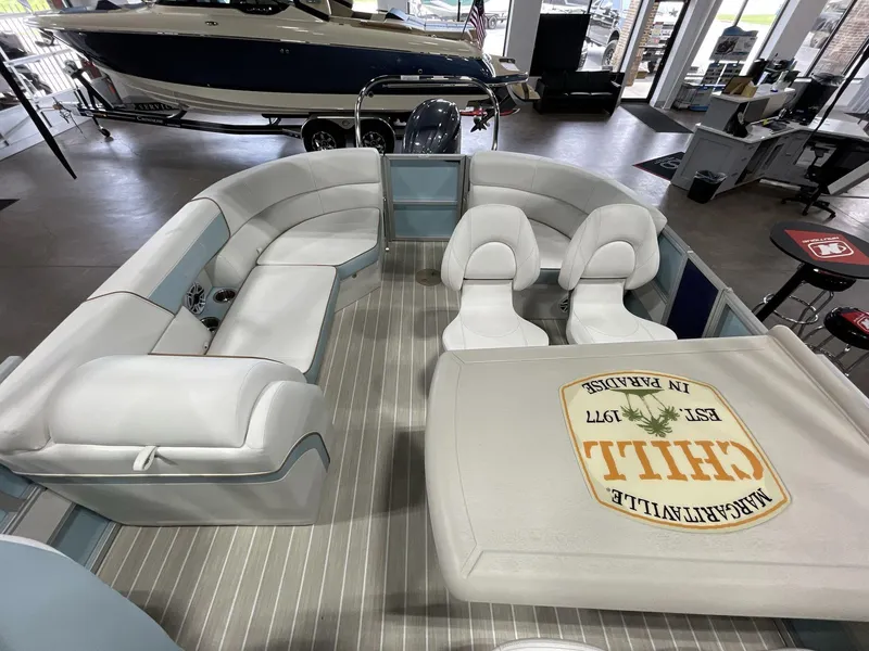 Slide: The Image of 2025 South Bay S224 Chill pontoon boat interior with white seating and table in showroom. - 14