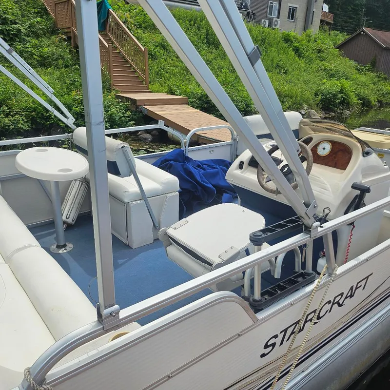 Slide: The Image of 2003 Starcraft Cruise 180 boat interior with seating and steering, docked near wooden stairs. - 4