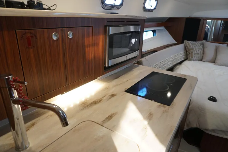 Slide: The Image of 2023 Pursuit OS 355 Offshore interior with kitchenette, featuring stove, microwave, and cozy seating area. - 39