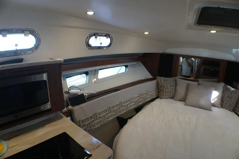 Slide: The Image of 2023 Pursuit OS 355 Offshore cabin interior with bed, windows, and kitchenette. - 46