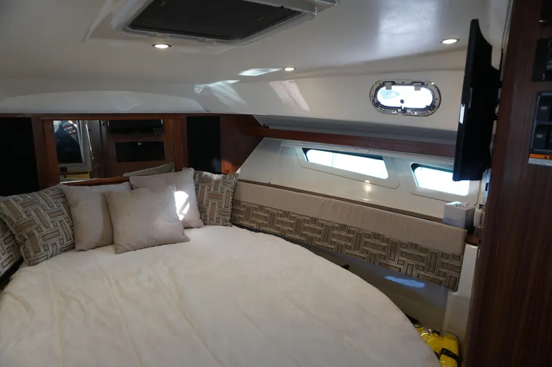 Slide: The Image of 2023 Pursuit OS 355 Offshore cabin interior with bed, pillows, and porthole windows. - 49