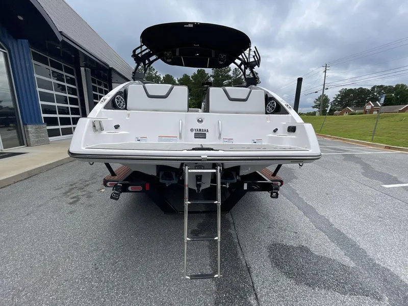 Slide: The Image of 2024 Yamaha Boats 252XE rear view with swim platform and ladder, parked outdoors. - 9