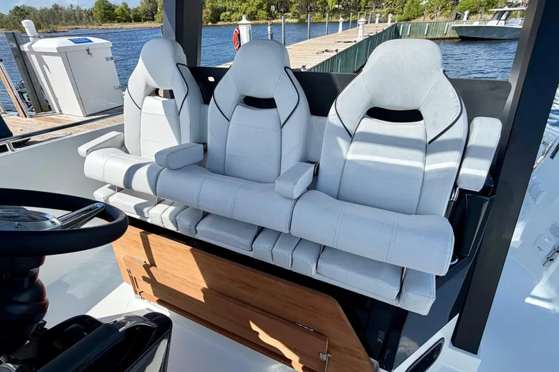 Slide: The Image of 2026 Beneteau Gran Turismo 35 cockpit with three white cushioned seats by the water. - 23