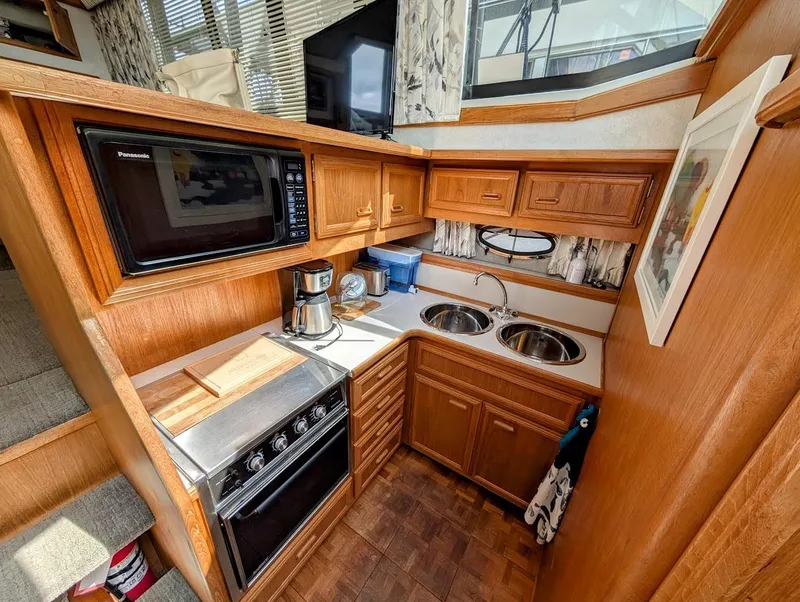 Slide: The Image of 1991 Carver 430 Cockpit Motor Yacht kitchen with wood cabinetry, microwave, stove, and dual sinks. - 15