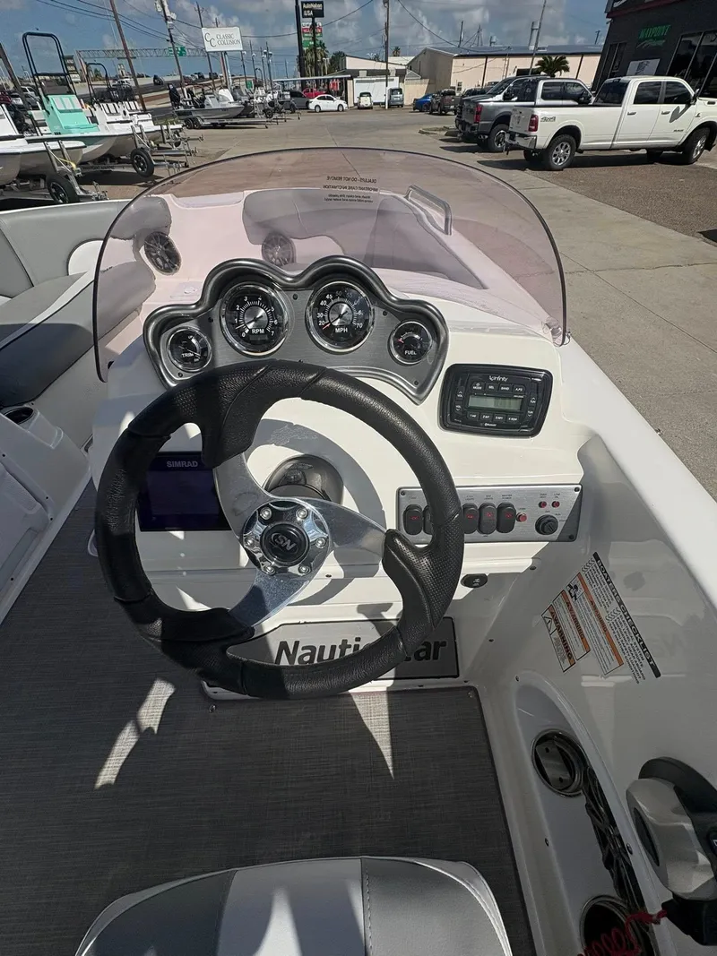 Slide: The Image of 2021 NauticStar 203 SC boat dashboard with steering wheel and gauges, parked outdoors. - 2