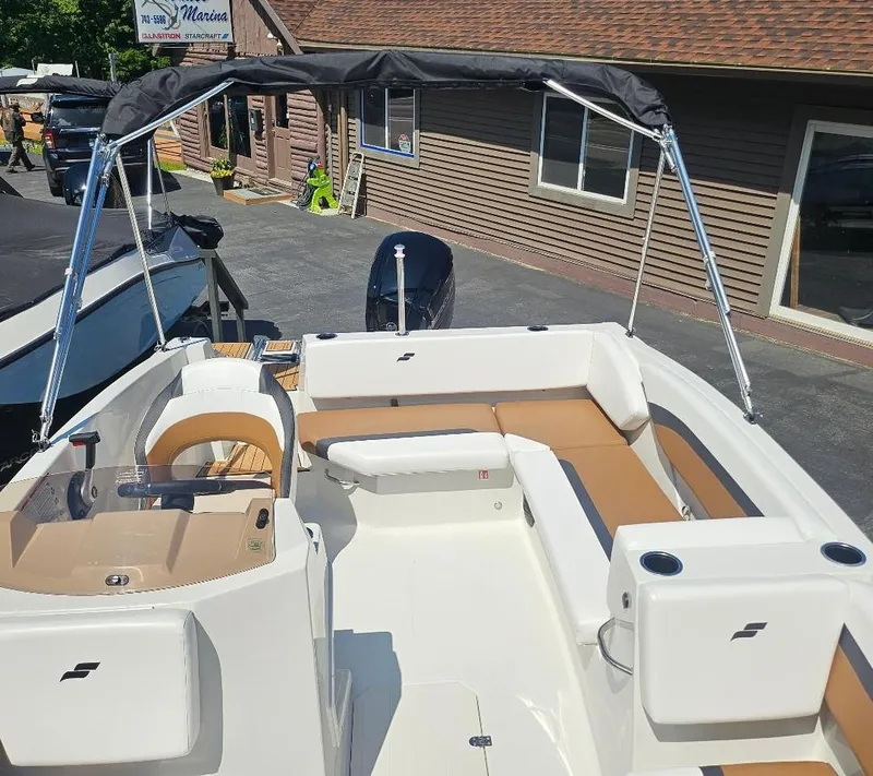 Slide: The Image of 2026 Starcraft SVX 171 OB boat with seating and canopy, parked near a building. - 9