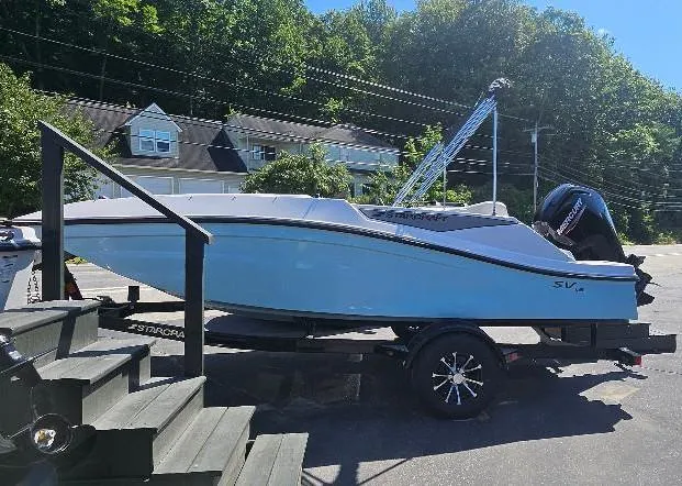 Slide: The Image of 2026 Starcraft SV 16 OB boat on trailer, parked outdoors, surrounded by trees and buildings. - 14