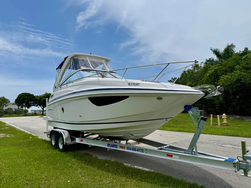 Slide: The Image of 2019 Regal 28 Express boat on trailer, parked on roadside with lush greenery. - 3