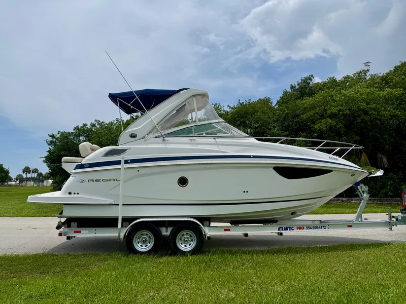 Slide: The Image of 2019 Regal 28 Express boat on trailer, parked outdoors with trees in background. - 4