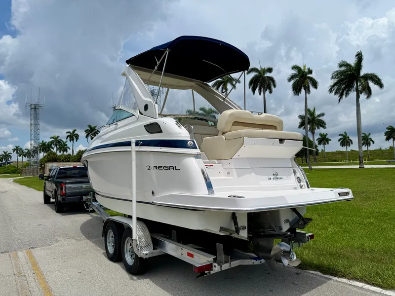 Slide: The Image of 2019 Regal 28 Express boat on trailer, parked roadside with palm trees and cloudy sky. - 7