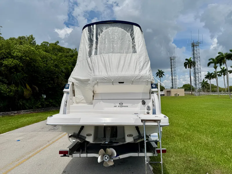 Slide: The Image of 2019 Regal 28 Express boat with cover, parked on a road near green grass and palm trees. - 8