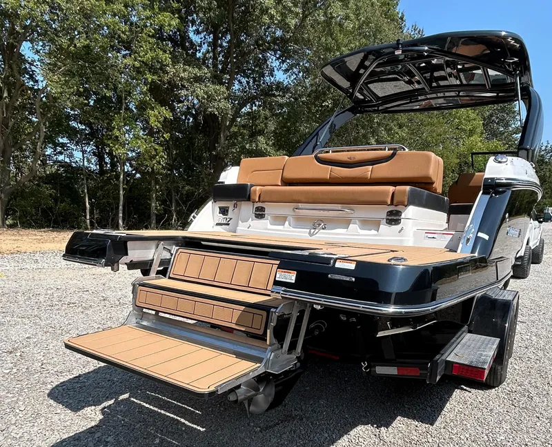 Slide: The Image of 2022 Chaparral 307 SSX boat with extended swim platform, parked on gravel, surrounded by trees. - 3