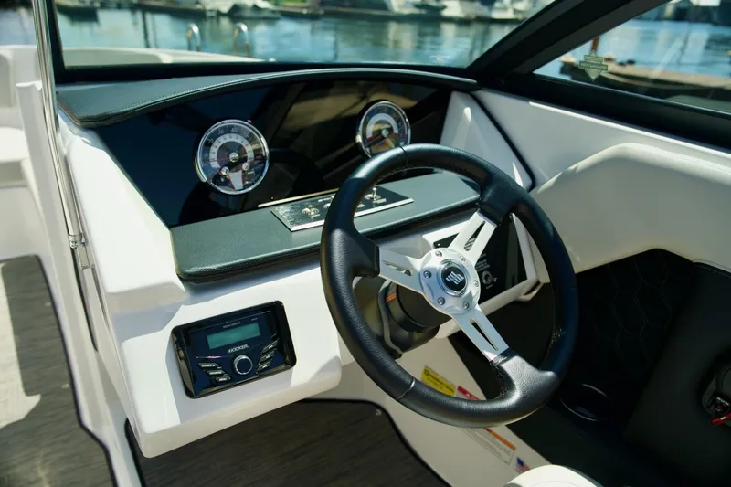 Slide: The Image of 2026 Four Winns H4 boat dashboard with steering wheel and gauges, docked by the water. - 7