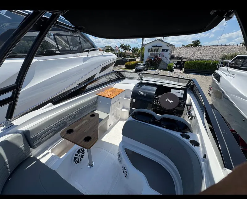 Slide: The Image of 2025 NX Boats NX270 interior with seating, helm, and wooden table in a marina setting. - 4