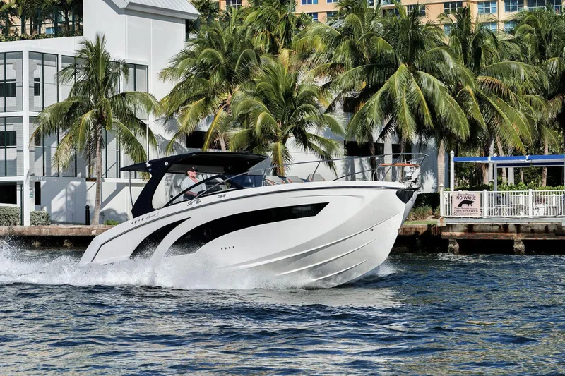 The Image of 2025 Hanover 377 Outboard boat cruising on water near palm trees and modern buildings. - 0