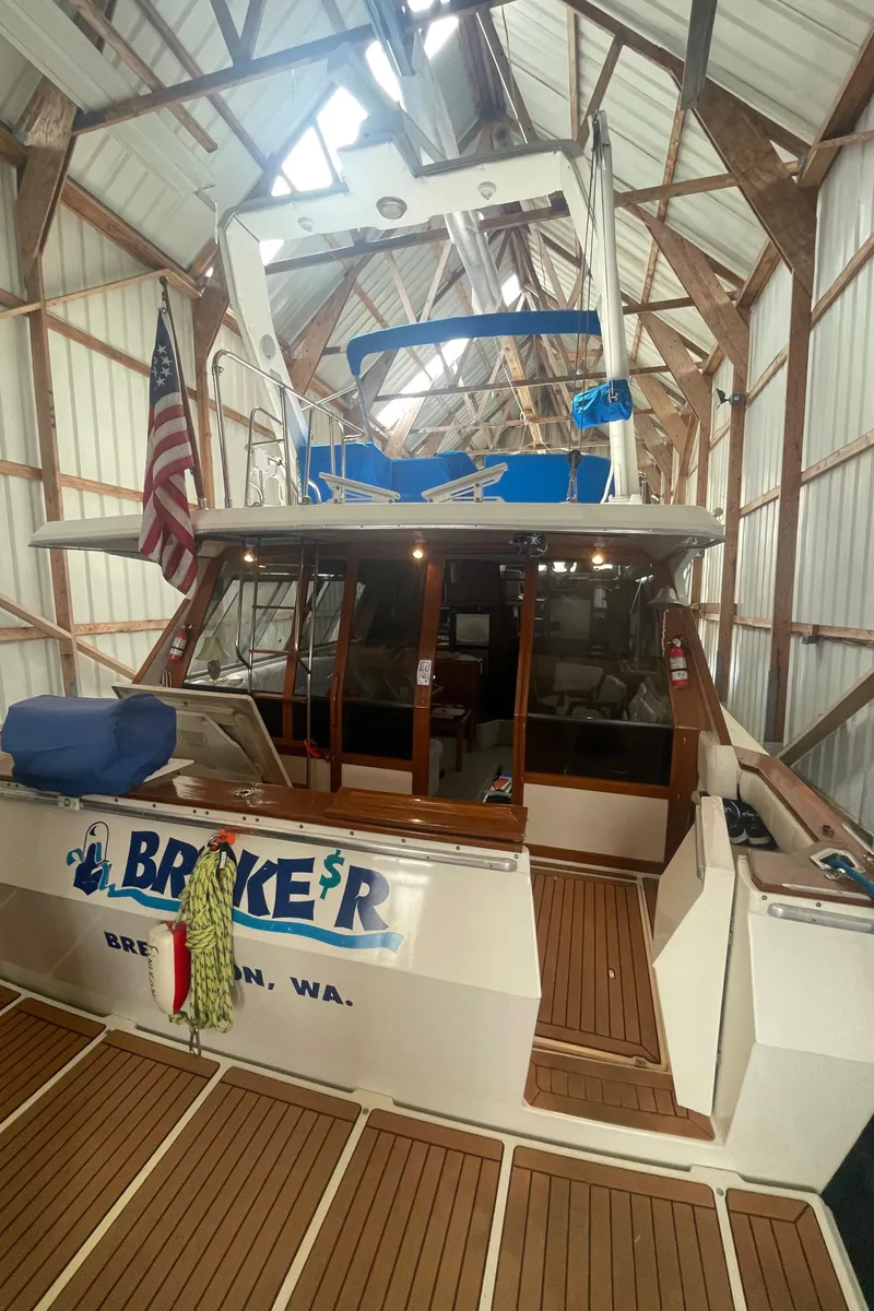 Slide: The Image of 1988 Bayliner 4588 yacht docked in a boathouse, featuring wooden deck and American flag. - 4