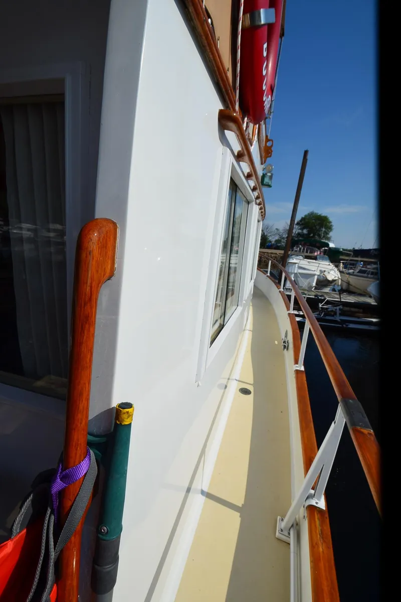 Slide: The Image of 1977 Grand Banks GB 32 yacht deck with wooden railings and docked boats in the background. - 30