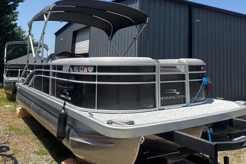 Slide: The Image of 2023 Bennington 22SX Swingback pontoon boat with canopy, parked near a metal building. - 10
