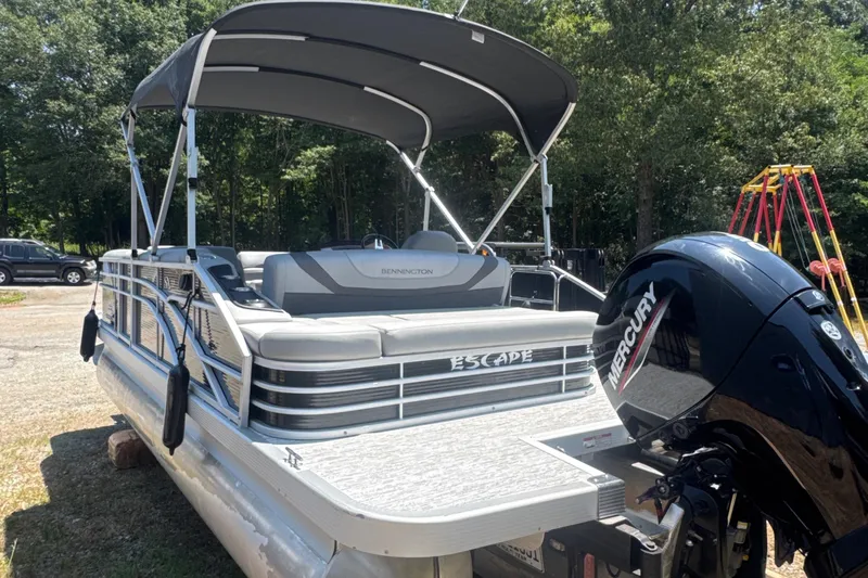 Slide: The Image of 2023 Bennington 22SX Swingback pontoon boat with Mercury engine, parked outdoors. - 5