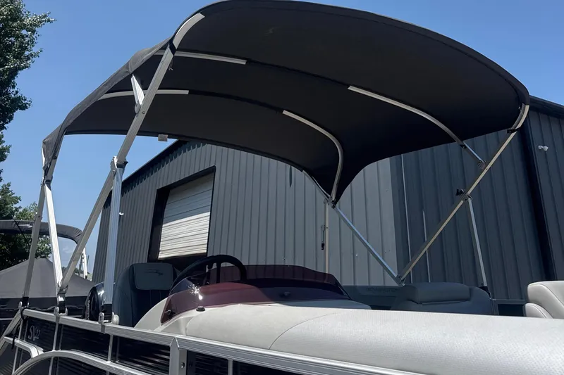 Slide: The Image of 2023 Bennington 22SX SWINGBACK pontoon boat with canopy, parked near a metal building. - 9