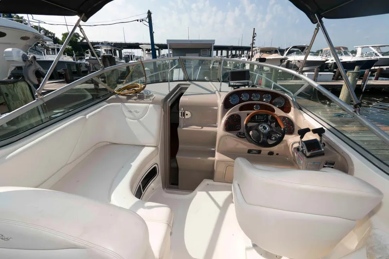 Slide: The Image of 2005 Sea Ray 280 Sundancer boat interior with helm, white seating, and docked marina view. - 6